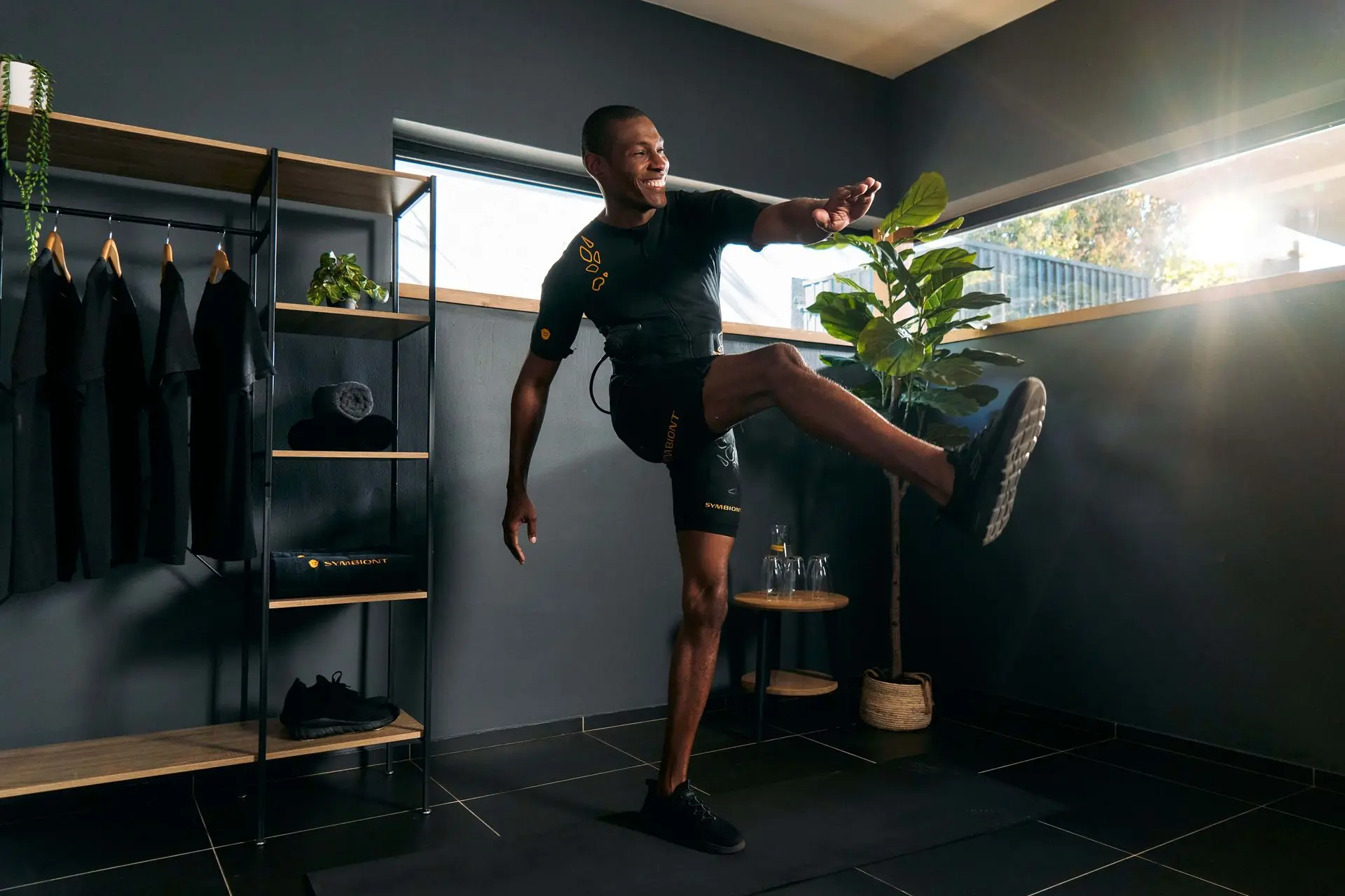 SYMBIONT EMS Experience – Die Zukunft der Fitness mit fortschrittlicher elektrischer Muskelstimulation Ein Mann im SYMBIONT EMS-Anzug führt eine Beinhebeübung aus. Der Raum ist lichtdurchflutet. Das Bild steht für die Zukunft des EMS-Trainings und der Fitness.