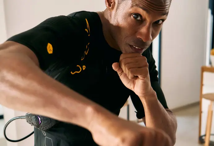 Maximieren Sie Ihr Training mit dem SYMBIONT Smart Training System - futuristisches Premium-EMS-Training Eine Person im SYMBIONT EMS-Anzug führt Boxbewegungen aus, mit einem konzentrierten Gesichtsausdruck. Das Bild steht für ein fortschrittliches Trainingserlebnis.